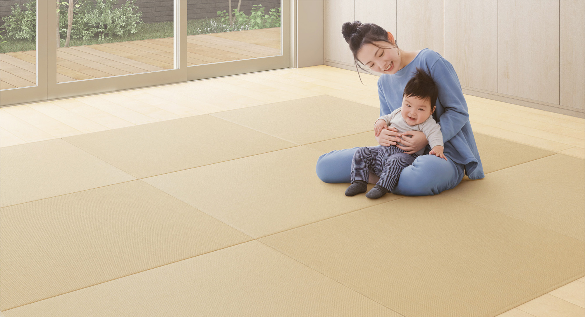 Mother sitting on the floor holding her smiling baby in a bright room with tatami mats.