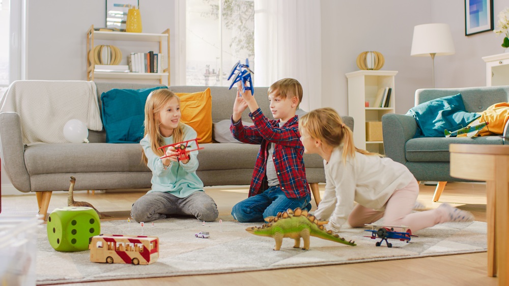 In the Living Room: Boy and Girl Playing with Toy Airplanes and Dinosaurs while Sitting on a Carpet. Sunny Living Room with Children Having Fun.