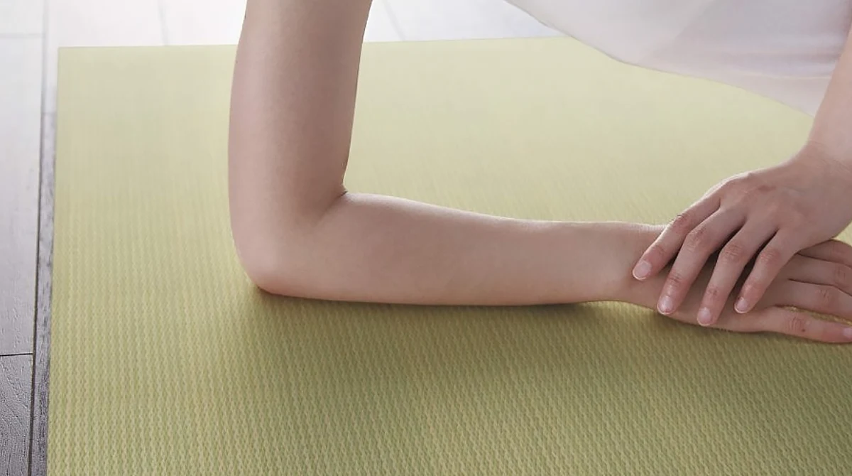 Close-up of a person's forearms resting on a light green textured tatami mat.
