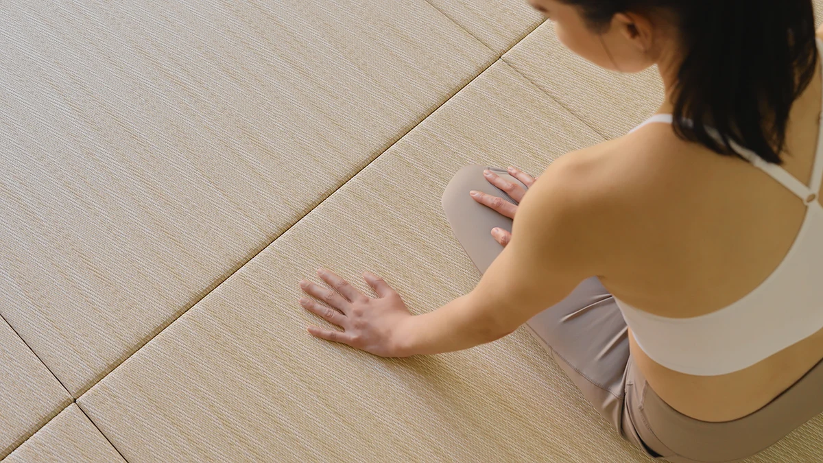 Overhead view of a woman in activewear sitting on light beige modular tatami mats.